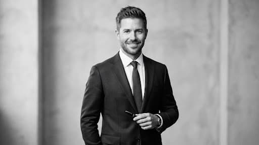 Studio black and white portrait of Julian Mercer, handsome male demand generation architect in his late 30s, sharp tailoring, neutral background, architectural lighting